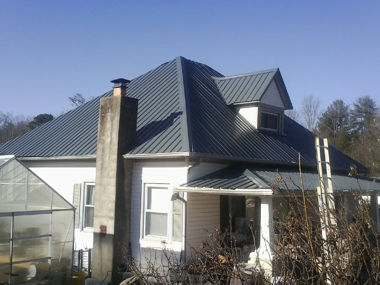 Dark blue standing seam metal roof on a white farmhouse with dormer — Slate & Tile Roof Repair by Roofing Brothers in Baldwinsville