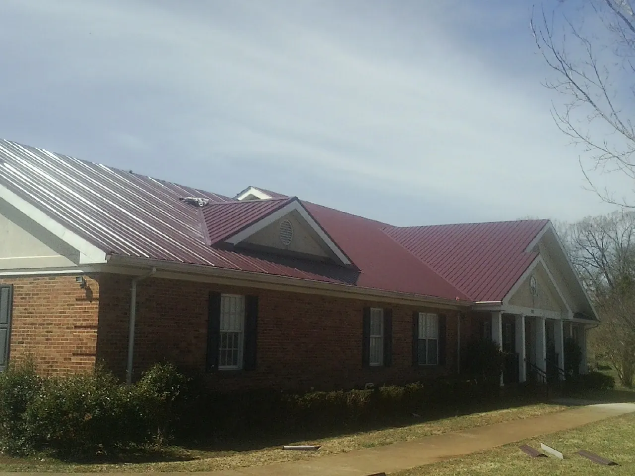 Red metal roof with gabled entries on a long brick building, from a Hail Damage Roof Repair job in Baldwinsville