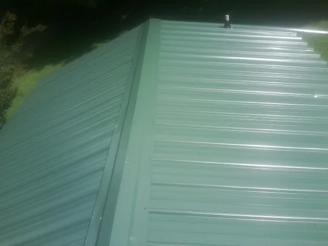New green metal panels meeting at the ridge of a roof — Flat Roof Repair work by our crew in Baldwinsville