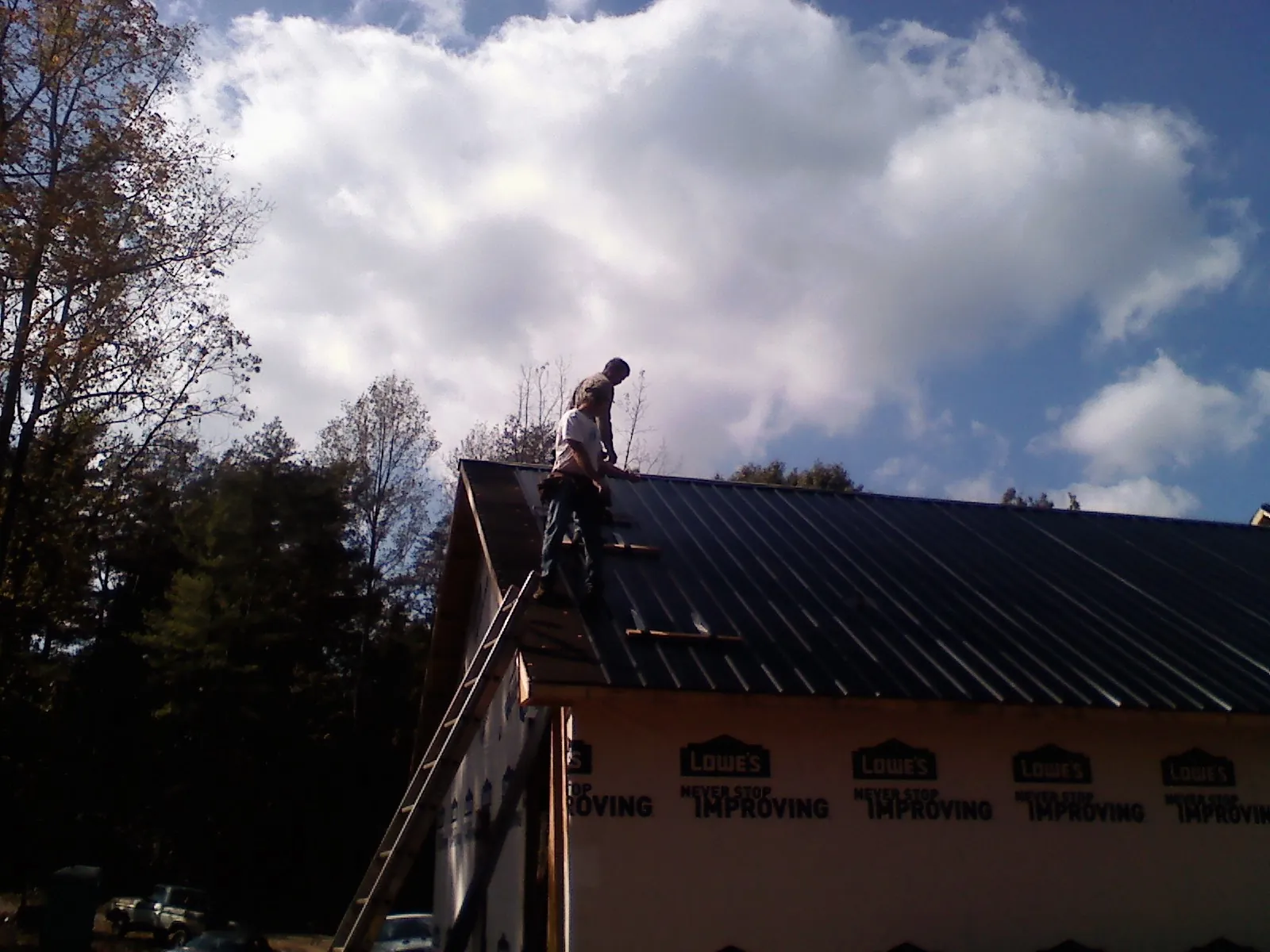 Roofer fastening dark metal panels high against a cloudy sky, from a Roof Inspection job in Baldwinsville