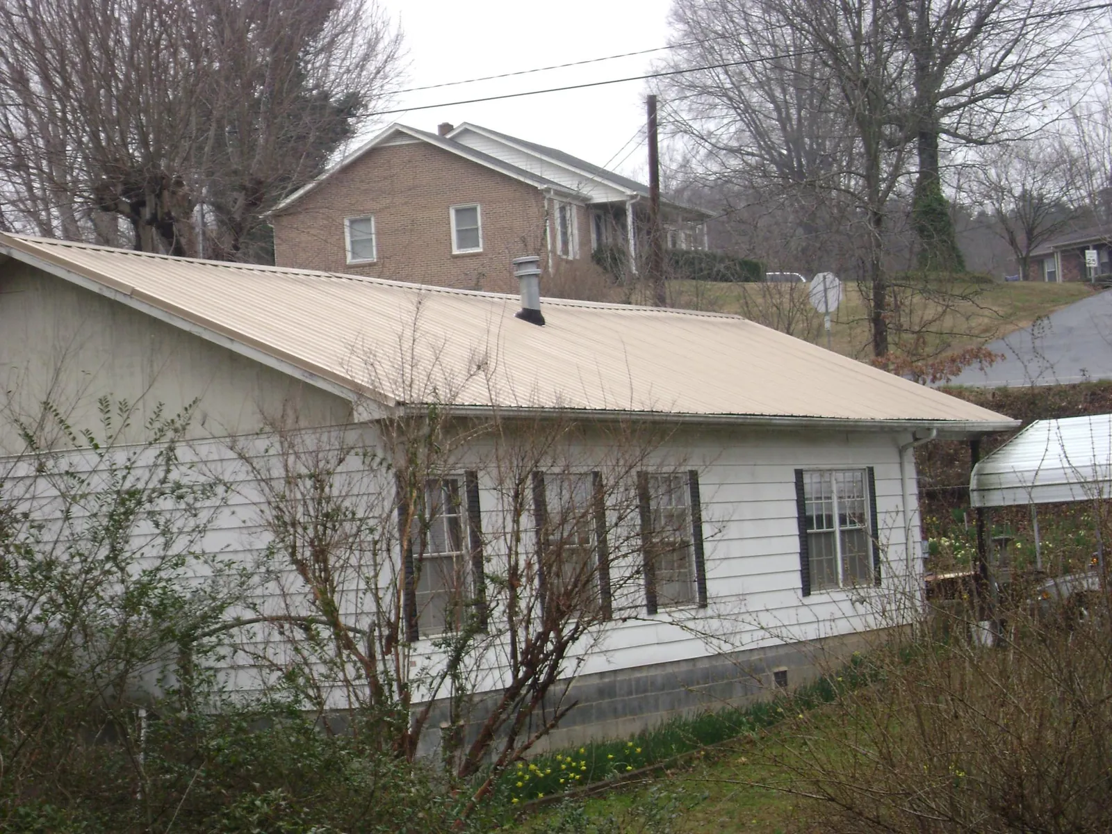 Tan metal roof on a white sided house set into a hillside — Commercial Roofing by Roofing Brothers in Baldwinsville